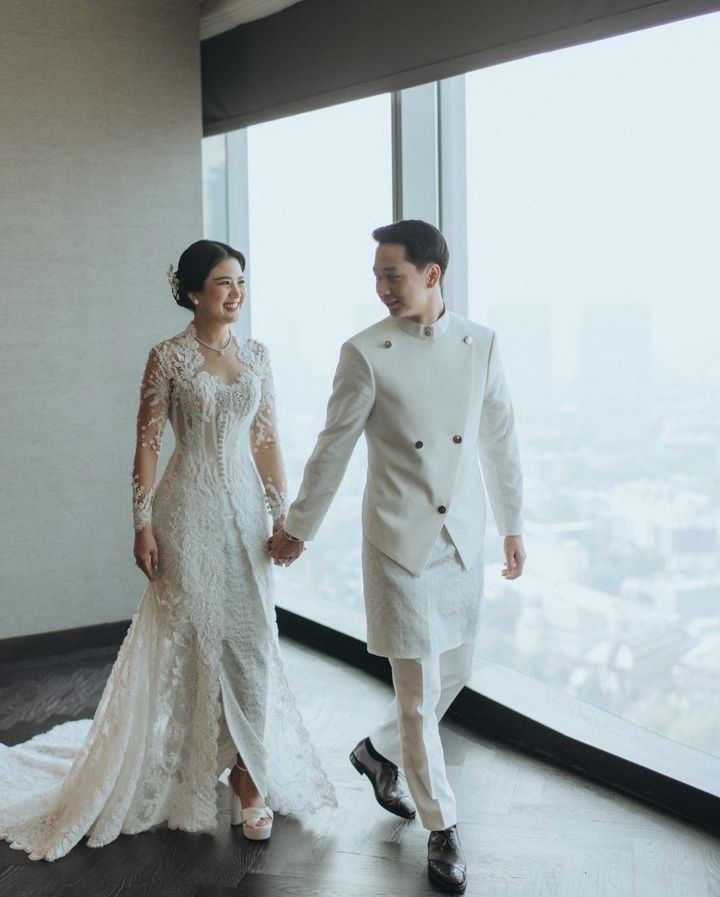 a bride and groom holding hands while standing in front of a window overlooking the city