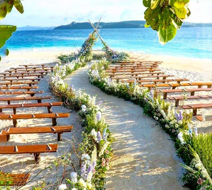 rows of wooden benches sitting on top of a sandy beach next to the ocean with flowers