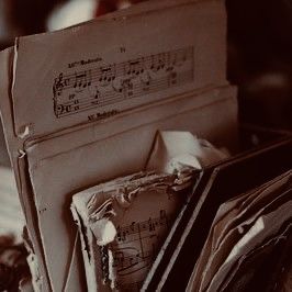 an open book sitting on top of a table next to a pile of music sheets