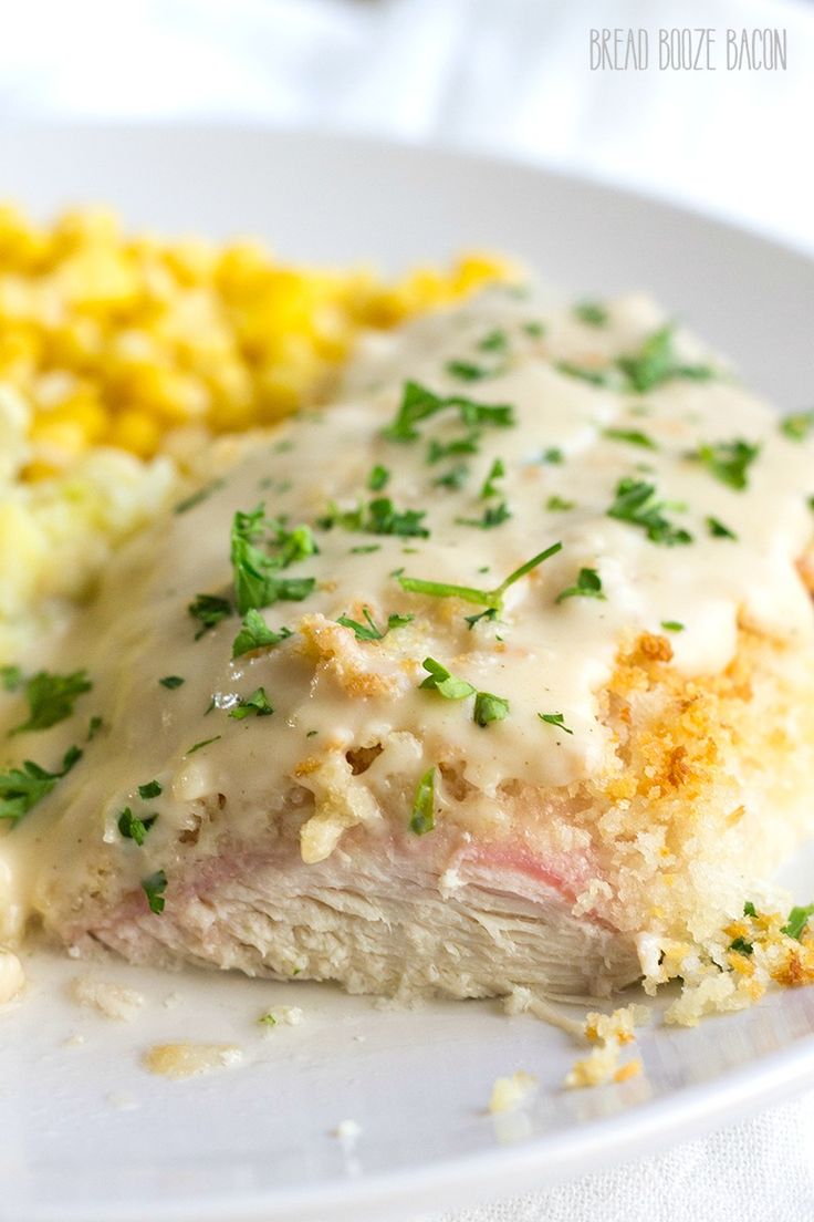 a white plate topped with meat covered in gravy next to corn