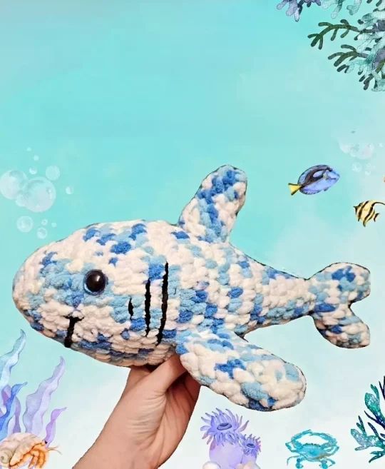 a hand holding a stuffed animal that looks like a fish with blue and white stripes