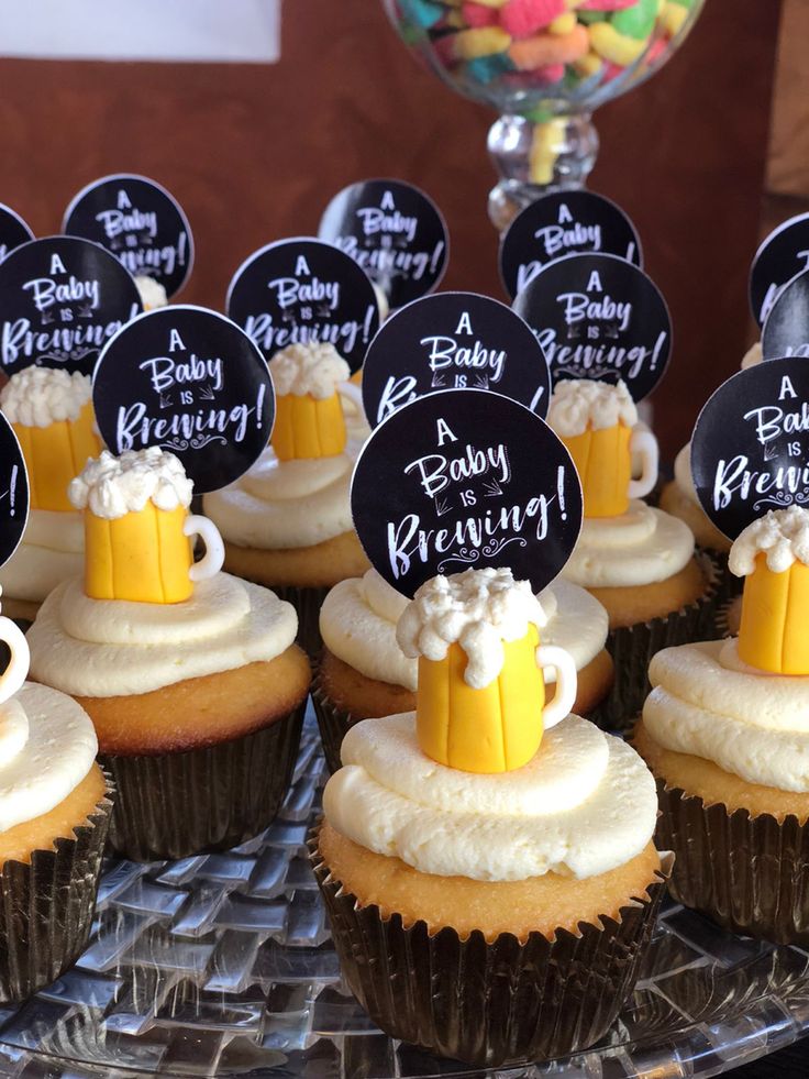 cupcakes decorated with frosting and topped with mini beer mugs are displayed on a platter