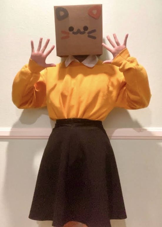 a person with a box on their head and hands in front of them, standing against a wall