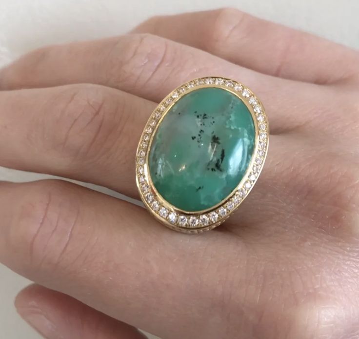 a woman's hand holding a ring with a large green stone in the middle