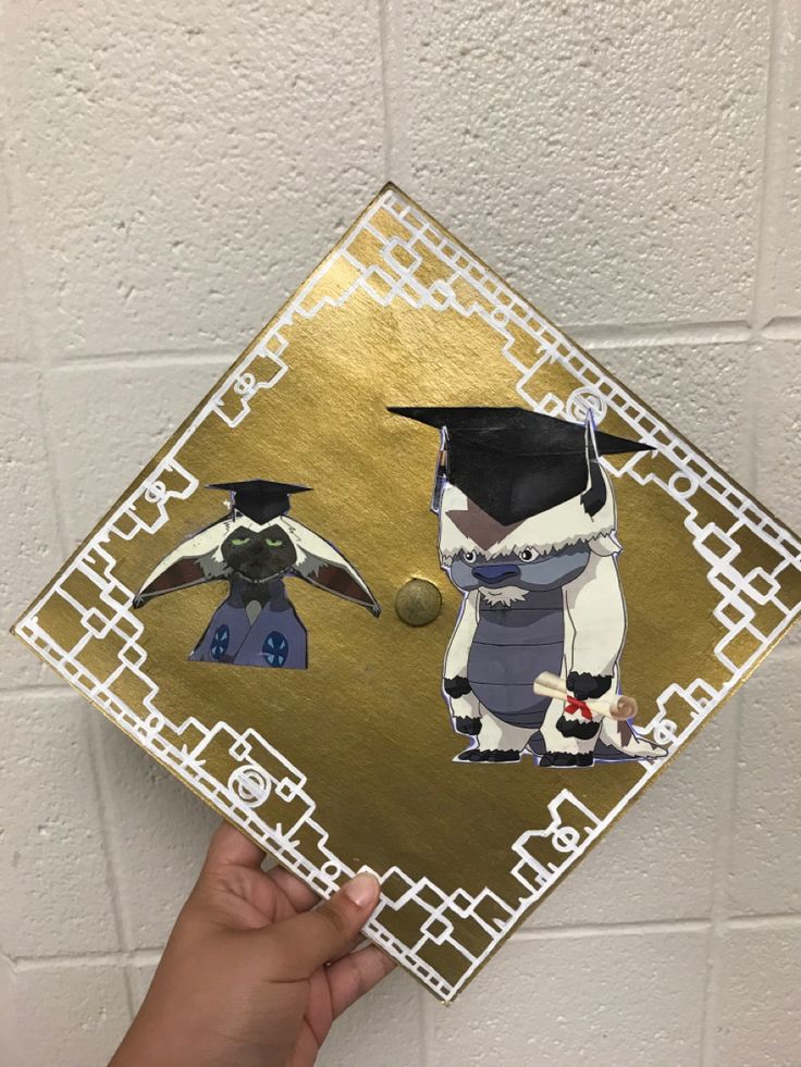 a hand holding up a graduation cap with an image of a bird and penguin on it