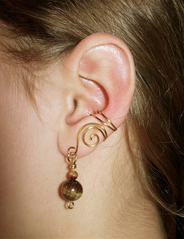 a woman's ear is adorned with gold wire and bead balls, which are dangling from the back of her ear