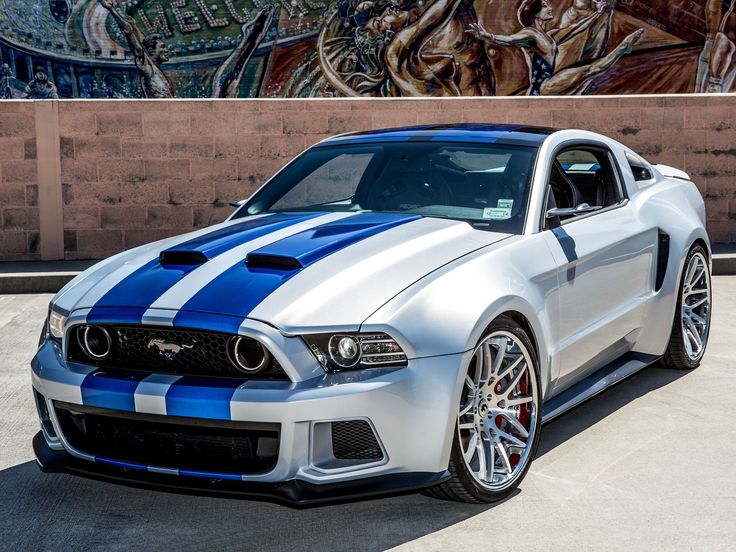 a white and blue mustang parked in front of a graffiti covered wall