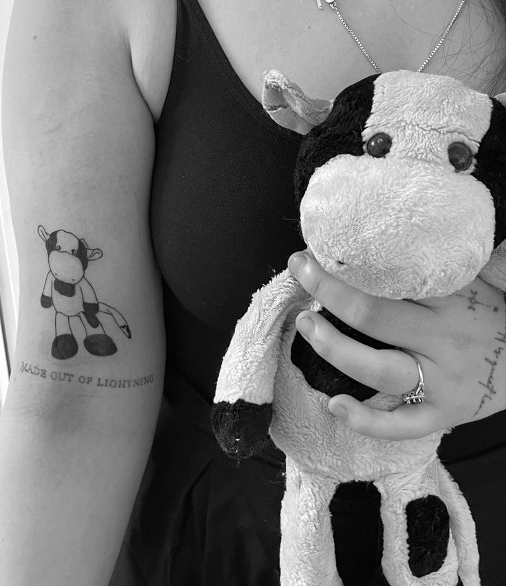 a woman is holding a stuffed cow in her hand and has a tattoo on it's arm