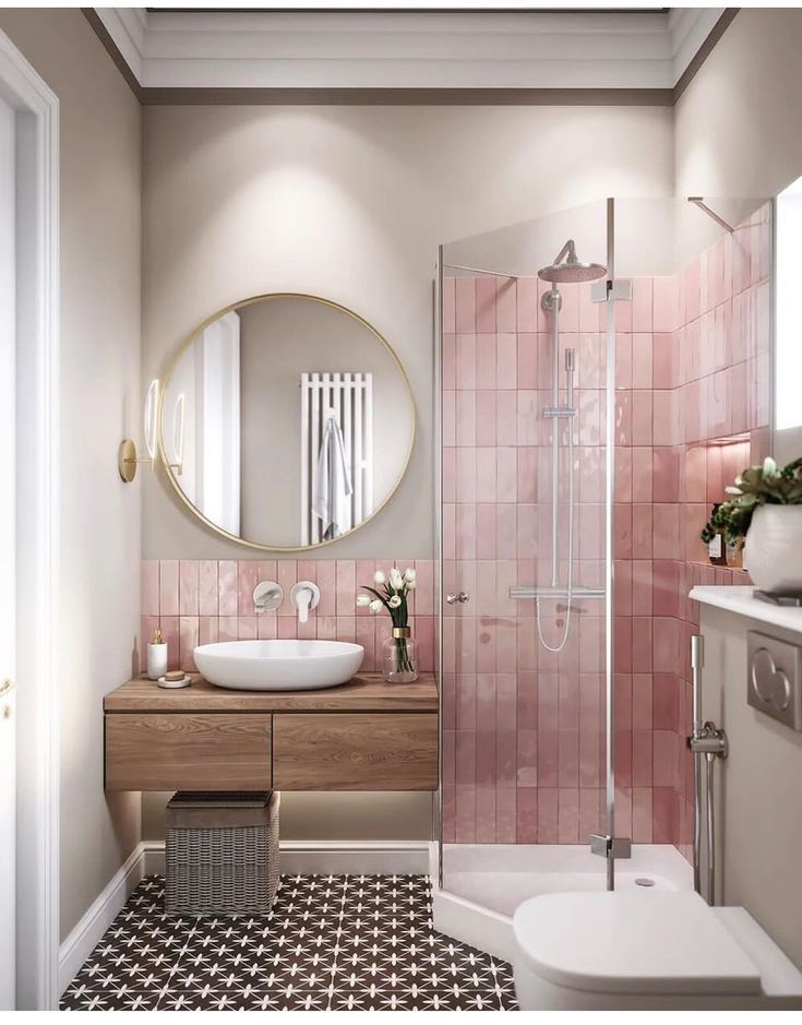 a bathroom with pink tiled walls and flooring, a round mirror above the sink