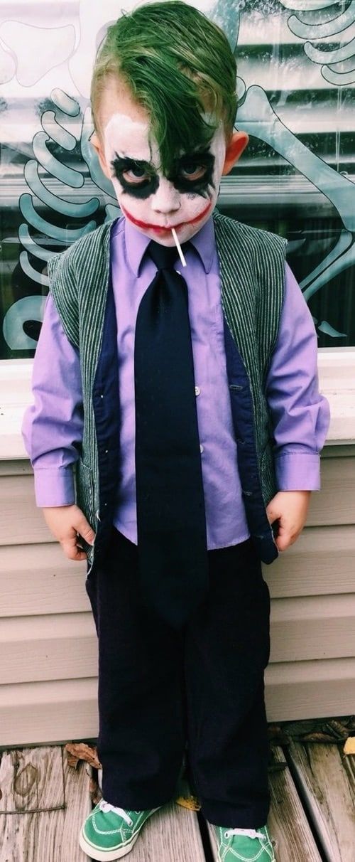 a little boy dressed up as the joker with his mouth open and tie undone, standing in front of a window