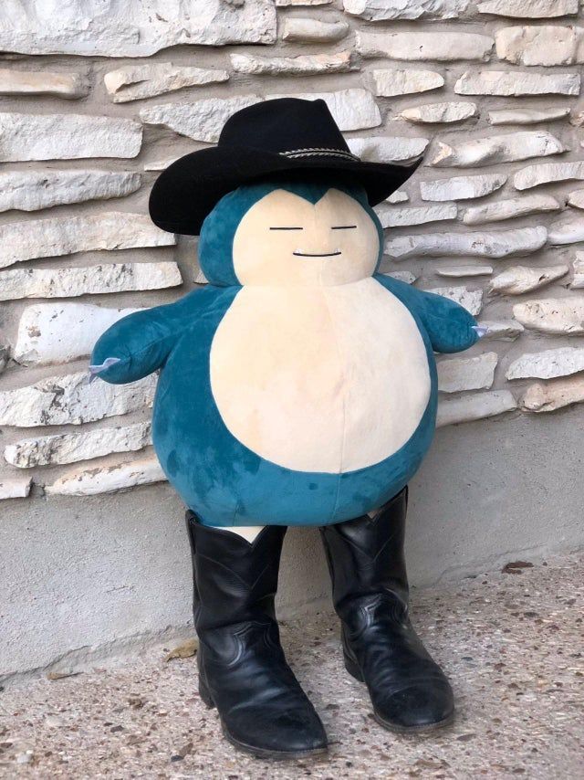 a large blue and white stuffed animal wearing a cowboy hat next to a stone wall