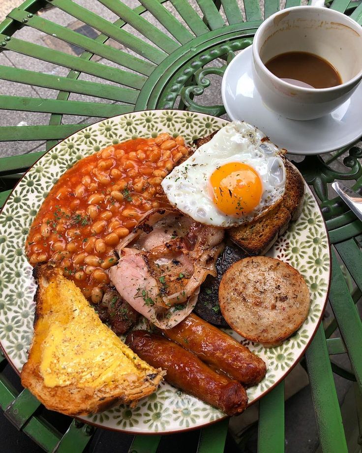 a plate with eggs, sausages and beans on it next to a cup of coffee