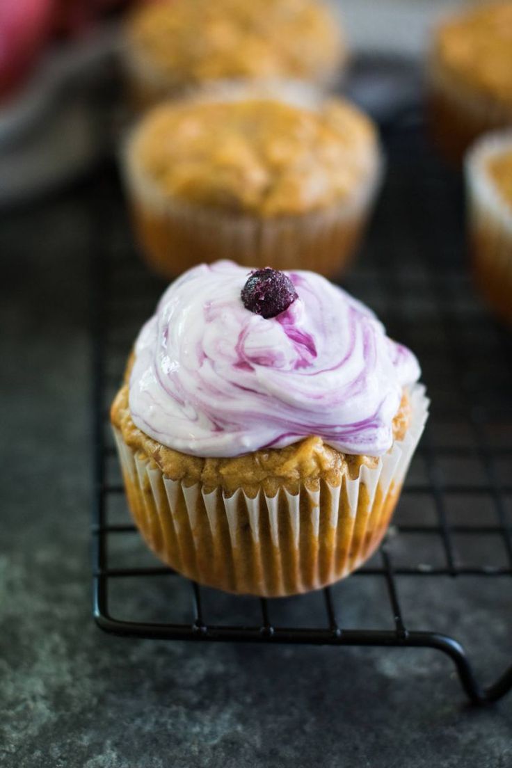 cupcakes with frosting and a berry on top are cooling on a wire rack