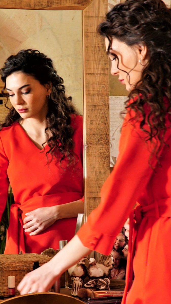 a woman in an orange dress is looking at her reflection in the mirror while another woman stands nearby