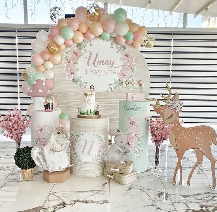 a table topped with cakes and balloons next to a deer statue on top of a marble floor