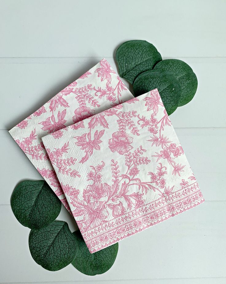 two pink and white napkins on top of green leaves next to each other,