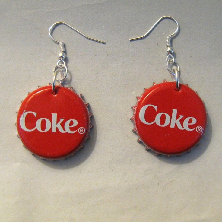 two coca - cola bottle caps with the word coke on them are hanging from silver earwires