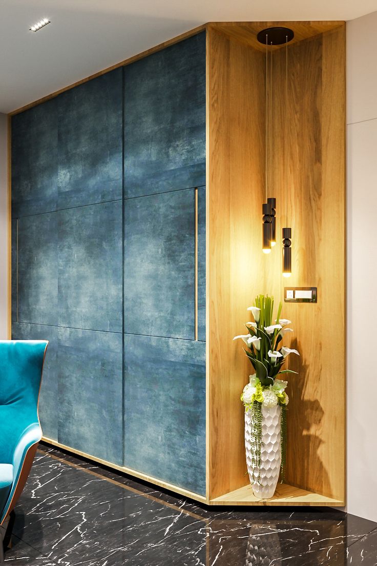 a blue chair sitting in front of a wooden cabinet with flowers on it and a vase next to it