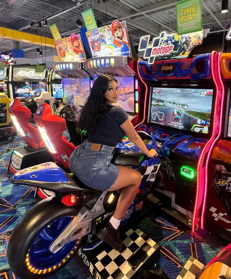 a woman riding on the back of a motorcycle next to a video game machine in a mall