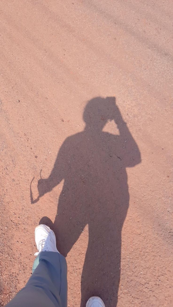 a person standing in the middle of a dirt road with their shadow on the ground