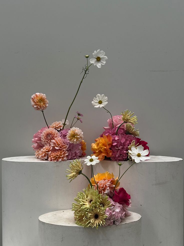 three white pedestals with flowers on them in front of a gray wall and floor