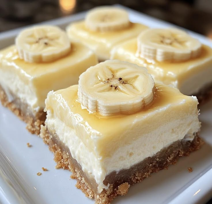 four slices of cheesecake with banana slices on top, sitting on a white plate