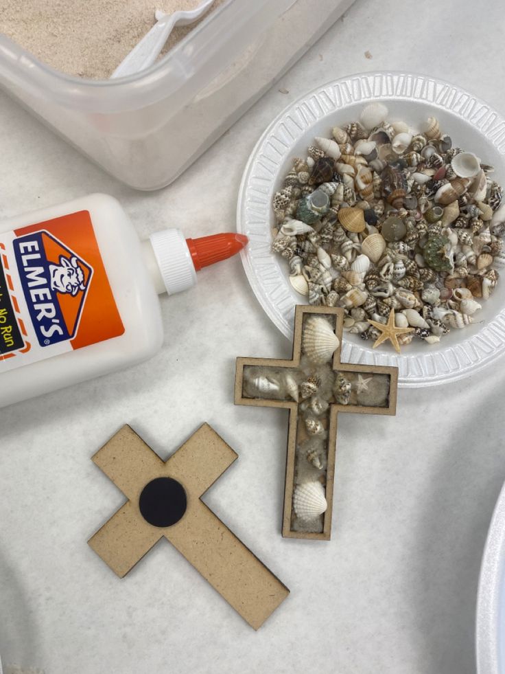 an assortment of seashells, sand and glue on a table with a cross