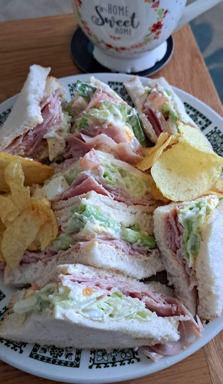 a white plate topped with a cut in half sandwich next to chips and a coffee cup