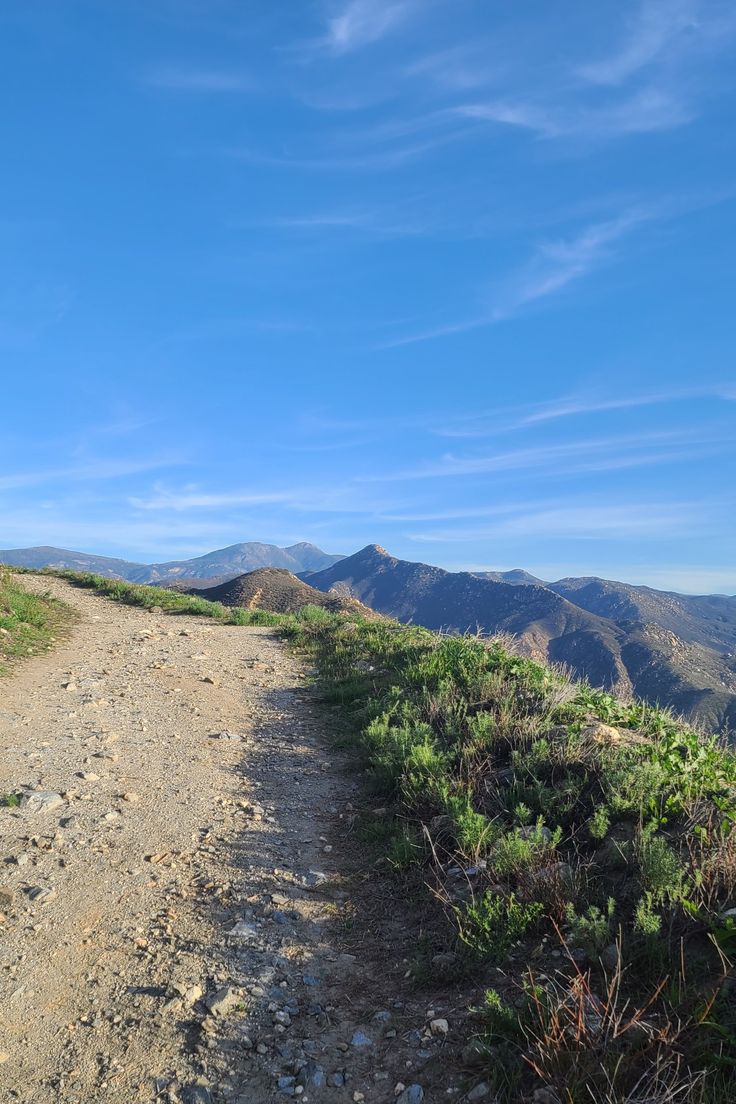 a dirt road going up the side of a hill with mountains in the back ground