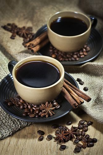 a cup of coffee surrounded by cinnamons and star anise on a black plate