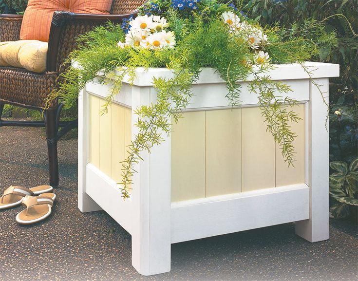 a white planter sitting on top of a wooden table next to a chair and flowers