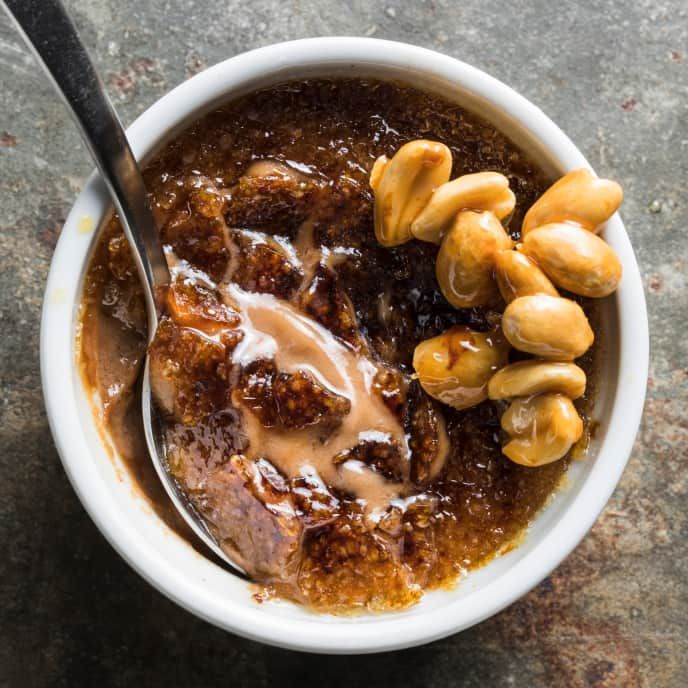 a white bowl filled with soup and nuts on top of a stone counter next to a spoon