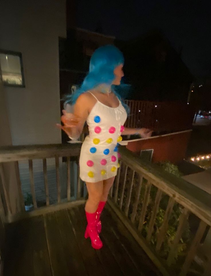 a woman with blue hair and polka dots on her dress is standing on a deck