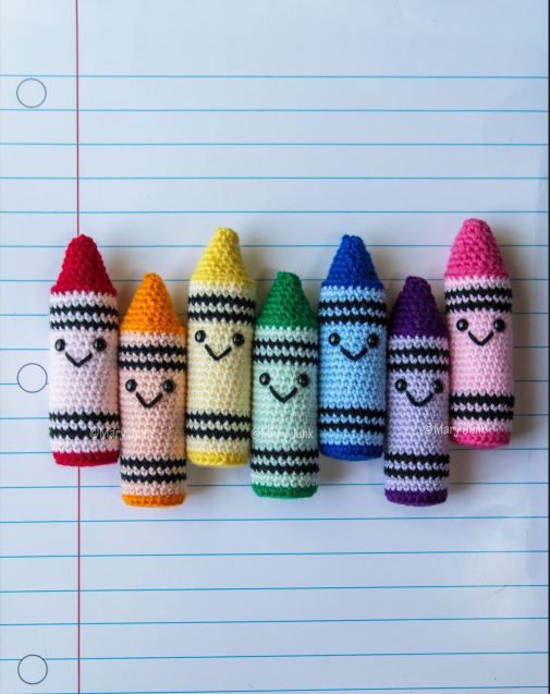 four crocheted crayons are lined up in a row with faces drawn on them