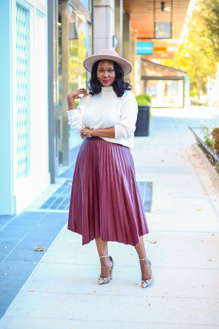 Pleated faux leather skirt with asymmetrical hemline. Pairs well with both fitted bodysuits and chunky sweaters. Styled here with our Sophia sweater and Sandy hat. Fabric: 55% PU, 45% Polyester Model is 5'6 and wearing a size medium. Fall Pleated Skirt Outfit, Maroon Skirt Outfit, Pleated Leather Skirt Outfit, How To Style Pleated Skirt, Burgundy Skirt Outfit, Pleated Skirt Outfit Ideas, Pleated Midi Skirt Outfit, Pleated Skirt Outfits, Maroon Skirt