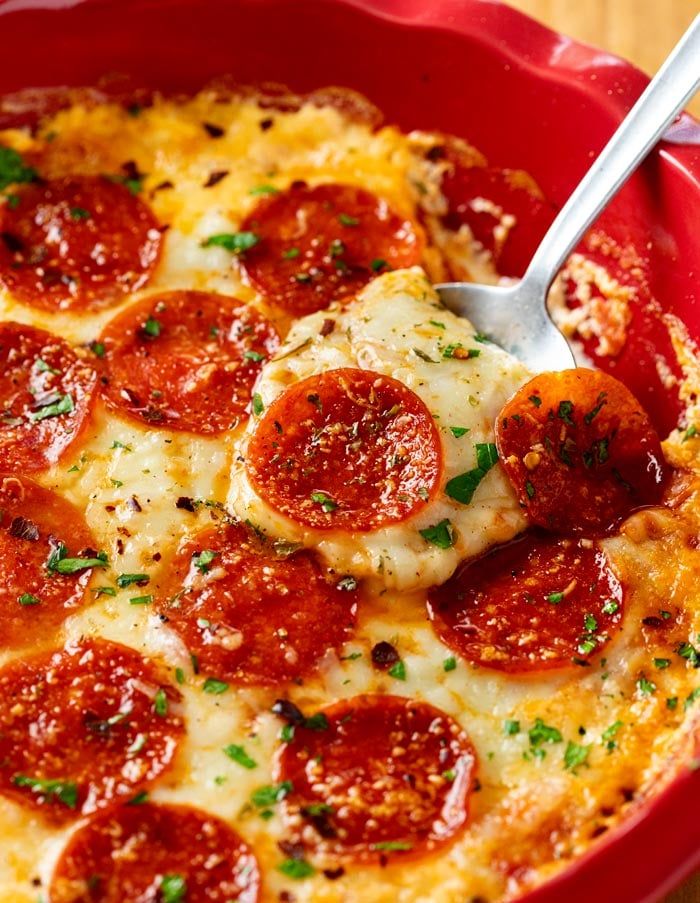 a pepperoni pizza casserole in a red dish with a spoon resting on it