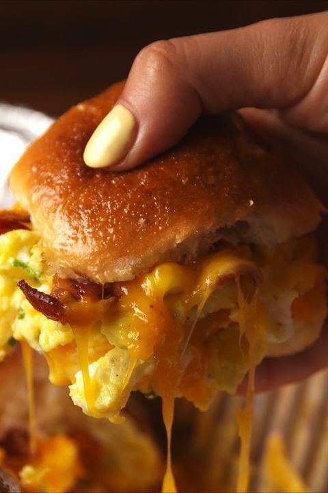 a person holding up a sandwich with eggs and cheese