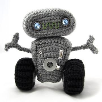 a gray crocheted robot toy with big wheels and two blue eyes sitting in front of a white background