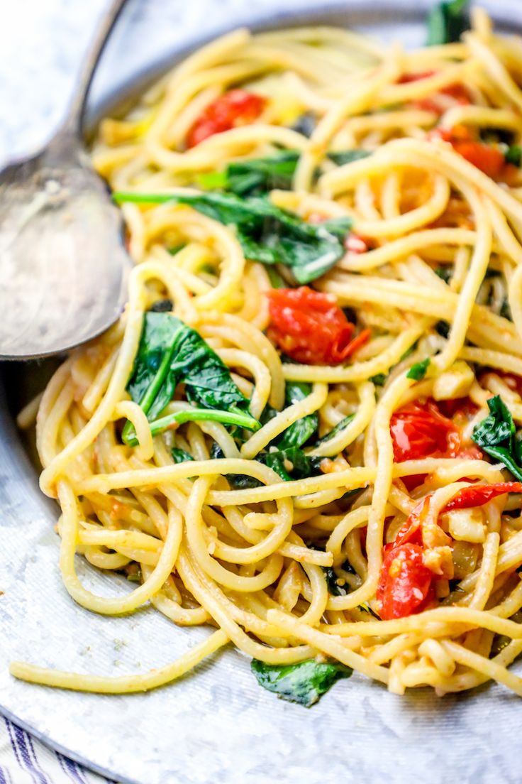 a plate of pasta with spinach, tomatoes and other toppings on the side