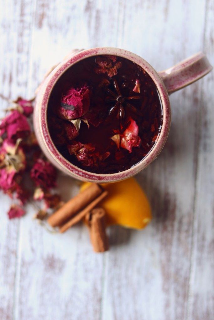 a cup filled with liquid next to some cinnamon sticks and flowers on a white table