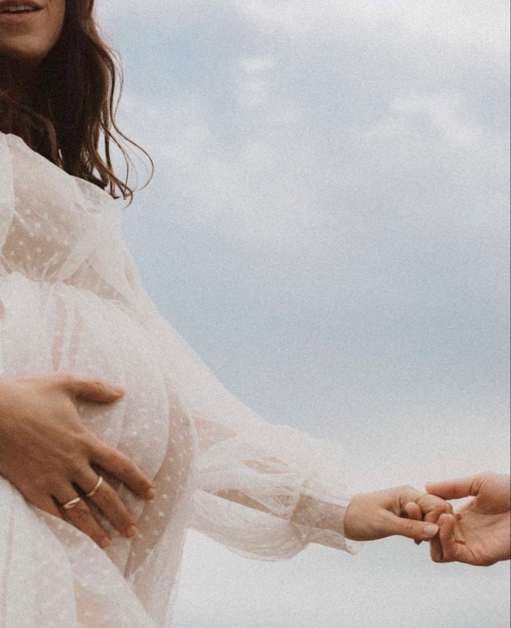 a pregnant woman is holding her hand out to another person's hand as they stand in the sky