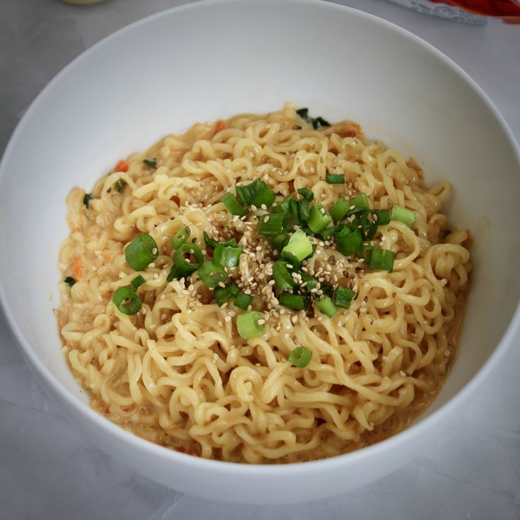 a white bowl filled with noodles and veggies on top of a marble table