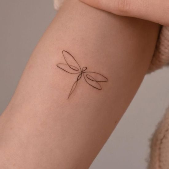 a woman's arm with a small dragonfly tattoo on the left side of her arm