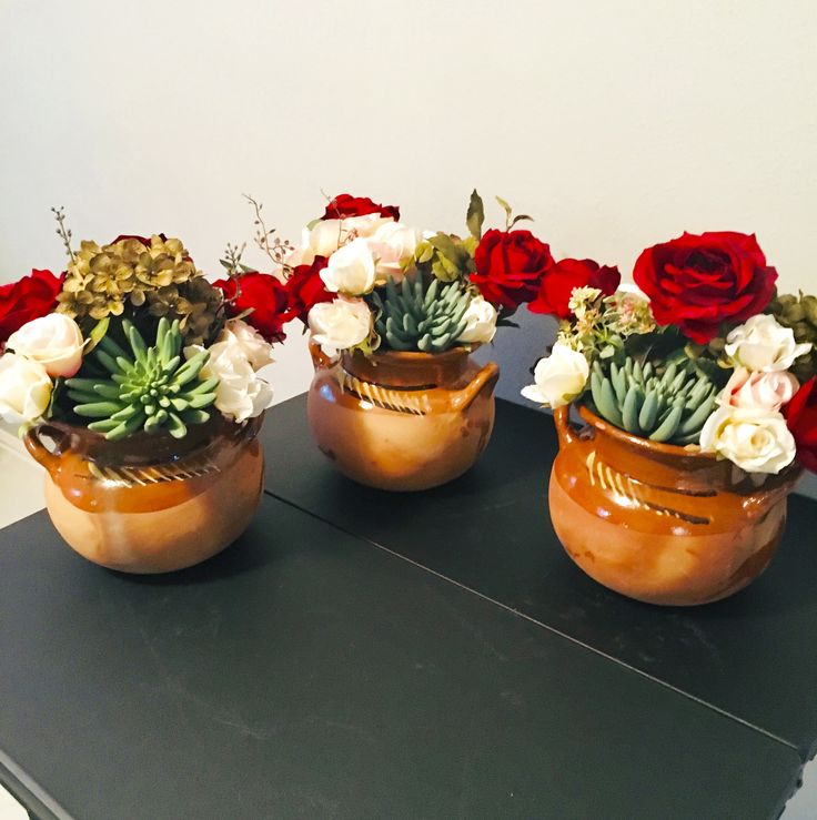 three vases filled with flowers sitting on top of a black table next to each other