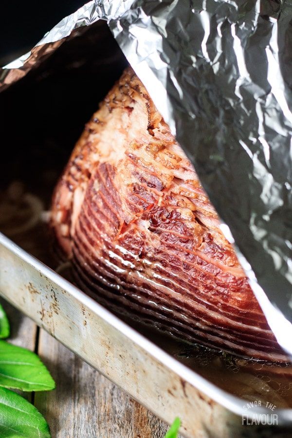 a piece of meat wrapped in tin foil on top of a wooden table next to green leaves