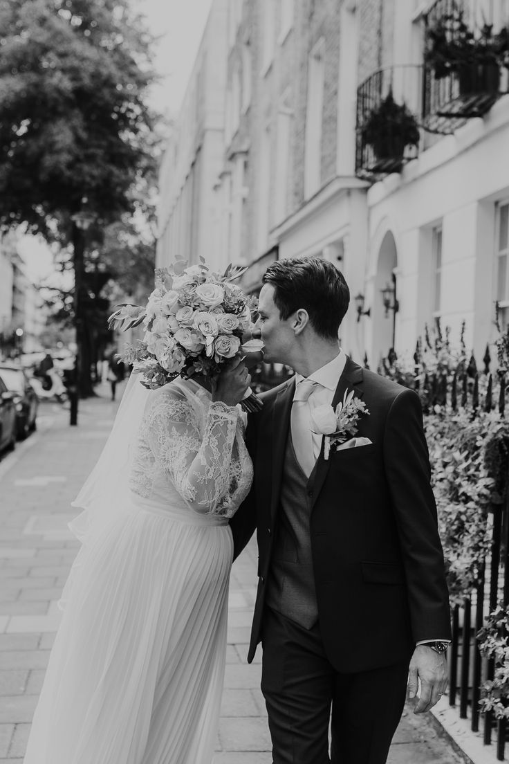 a bride and groom are walking down the street in black and white, holding each other's hand