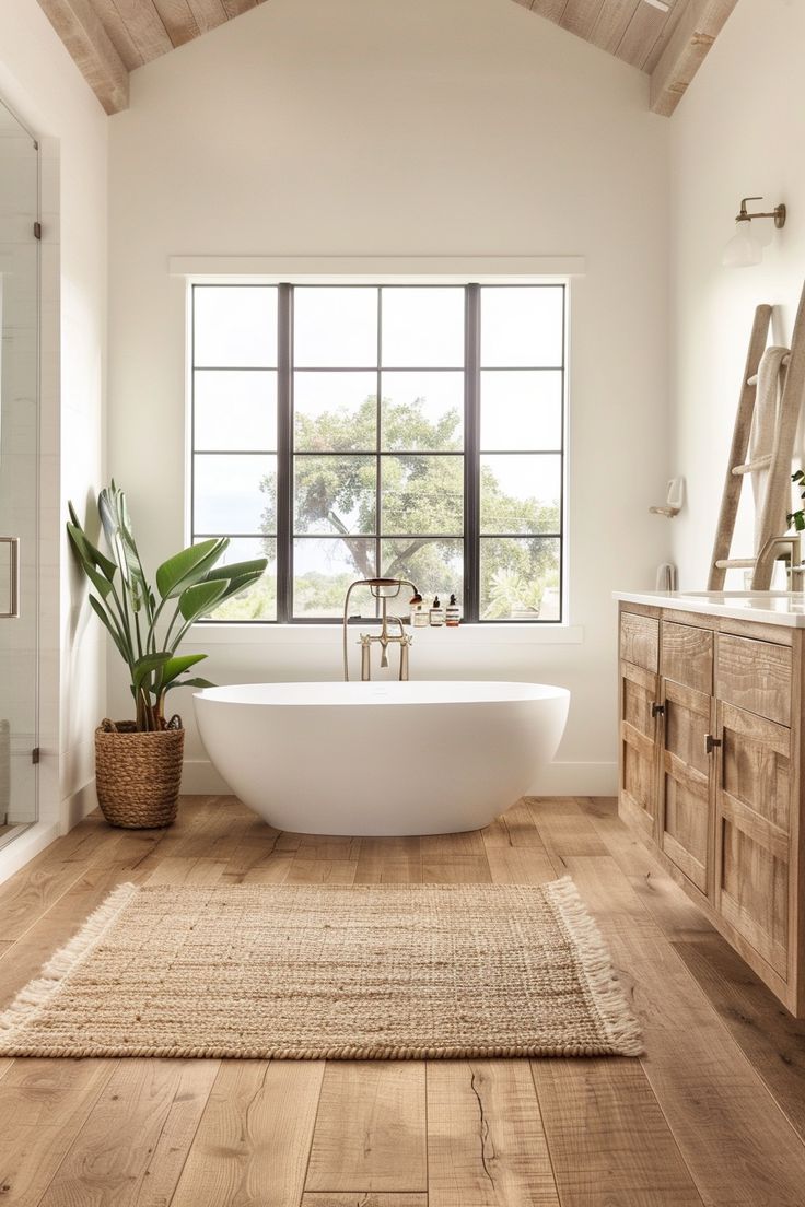 a bathroom with a large white tub and wooden flooring next to a tall window