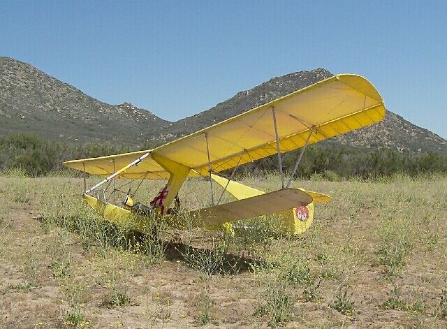 a small yellow airplane sitting in the middle of a field with mountains in the background