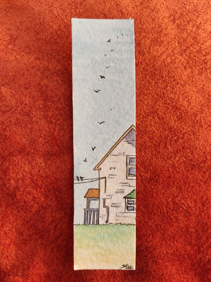 a bookmark with an image of a house and birds flying over it on a red surface