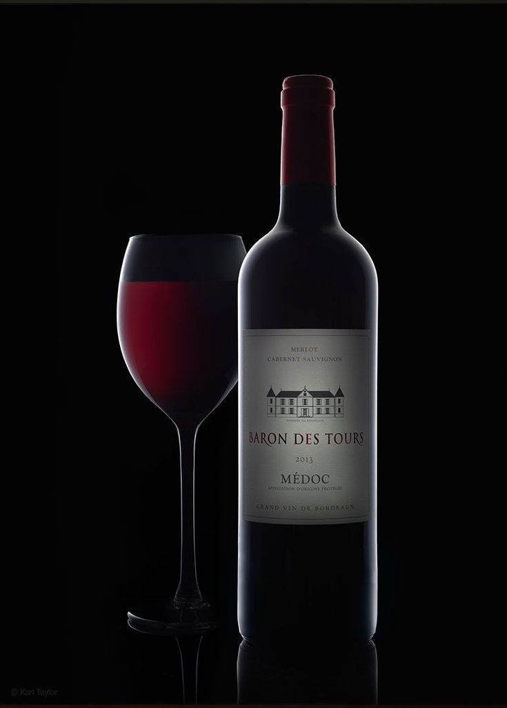 a bottle of wine next to a glass on a black surface with a dark background